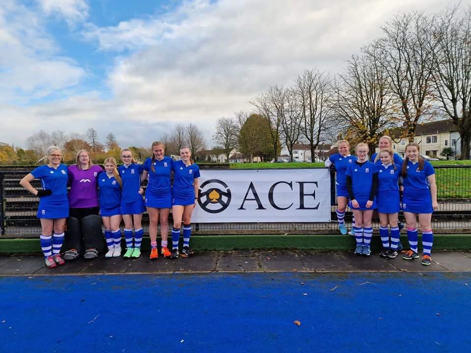 Antrim Ladies Hockey Club team with Ace Cabs sponsorship banner on the pitch