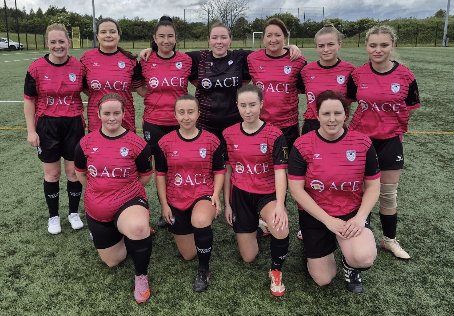 Antrim Town Women and Girls FC Swifts team in Ace Cabs sponsored pink kits on the pitch